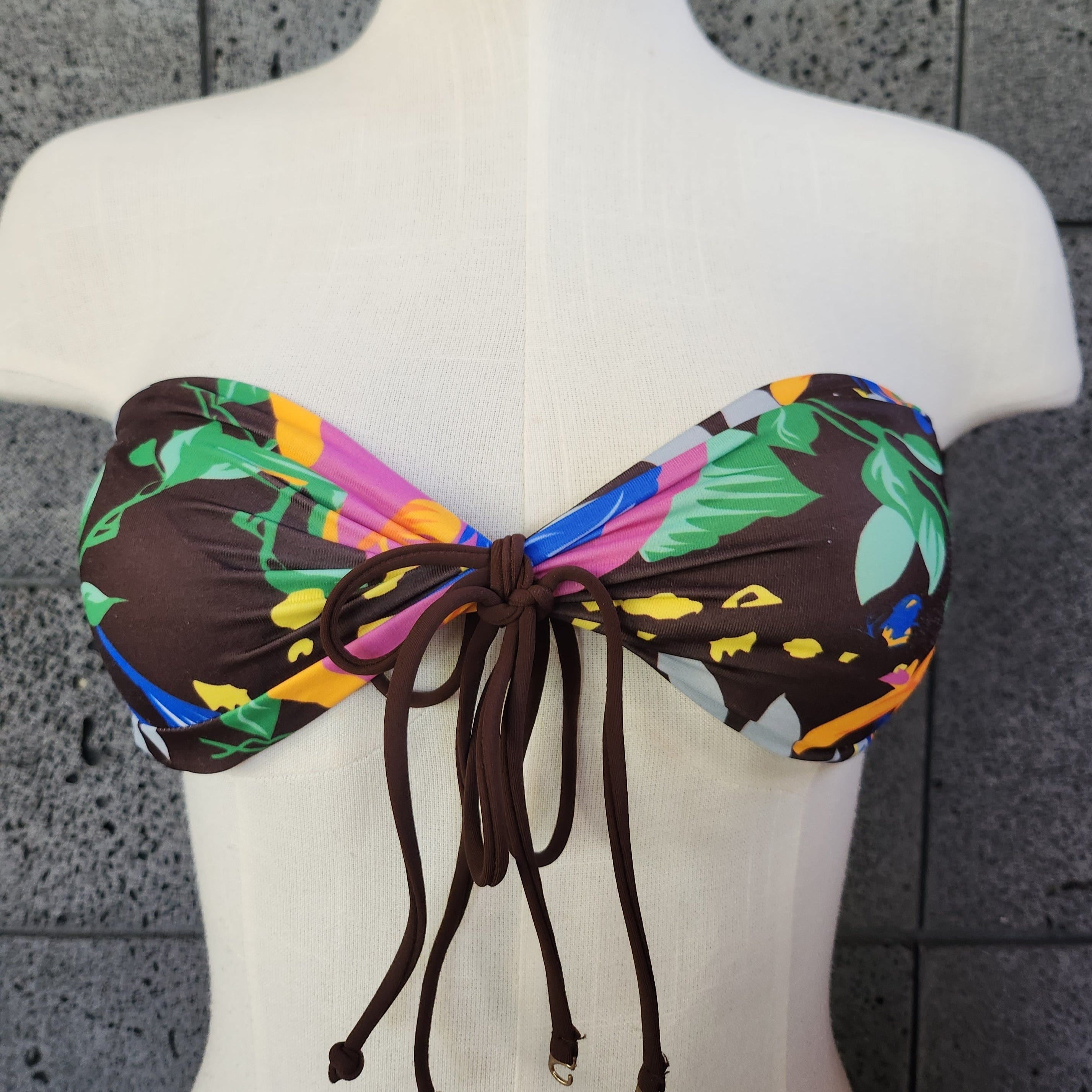 This image features the Loco Boutique Aloha Friday Bandeau Bikini Top, part of a stylish swimwear set. The bandeau top displays a vibrant tropical bloom print with a mix of green leaves, orange blooms, and blue accents, creating a fresh and colorful look.