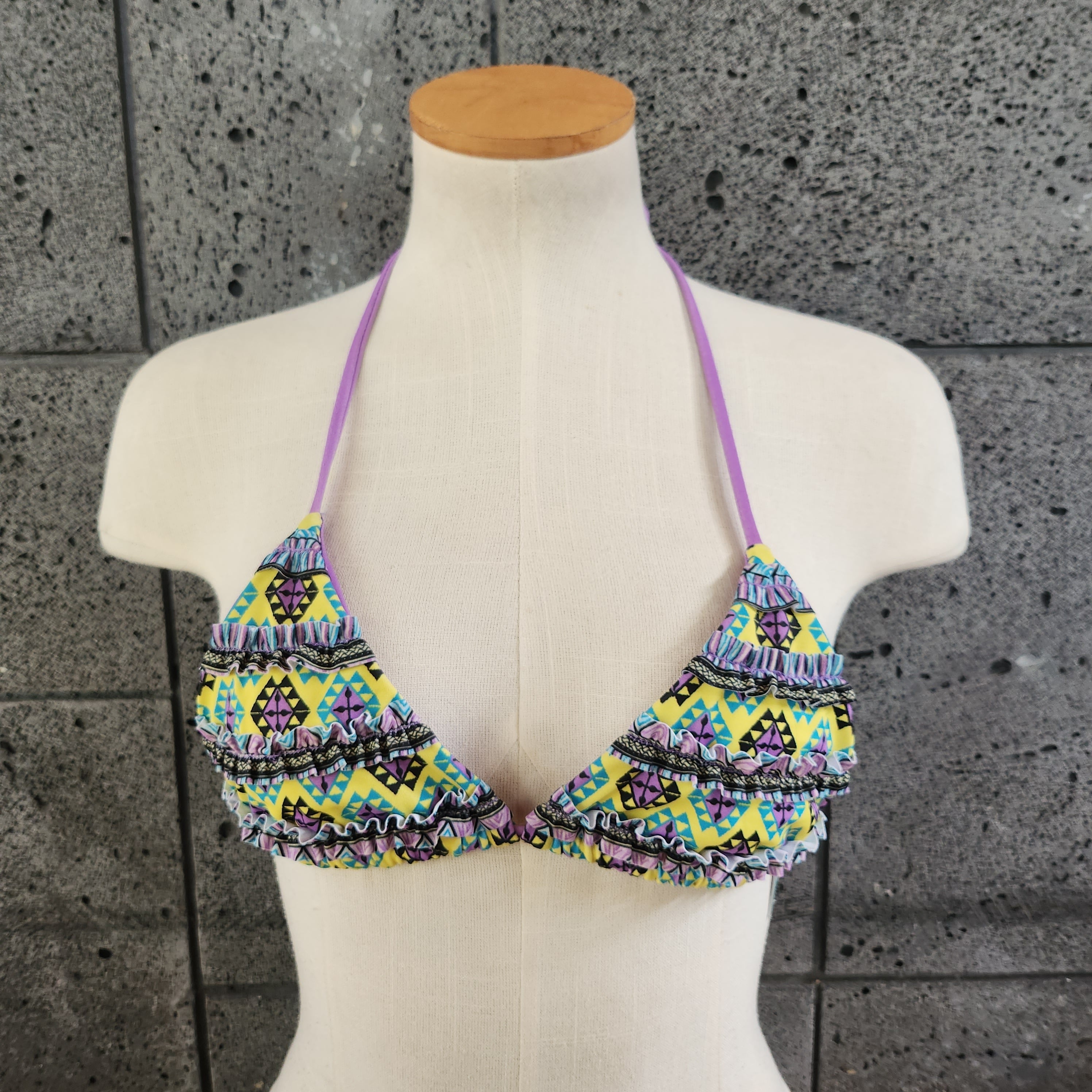Colorful triangle bikini top on a mannequin against a gray tiled wall.