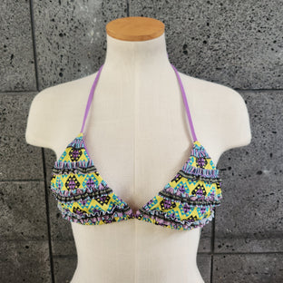 Colorful triangle bikini top on a mannequin against a gray tiled wall.