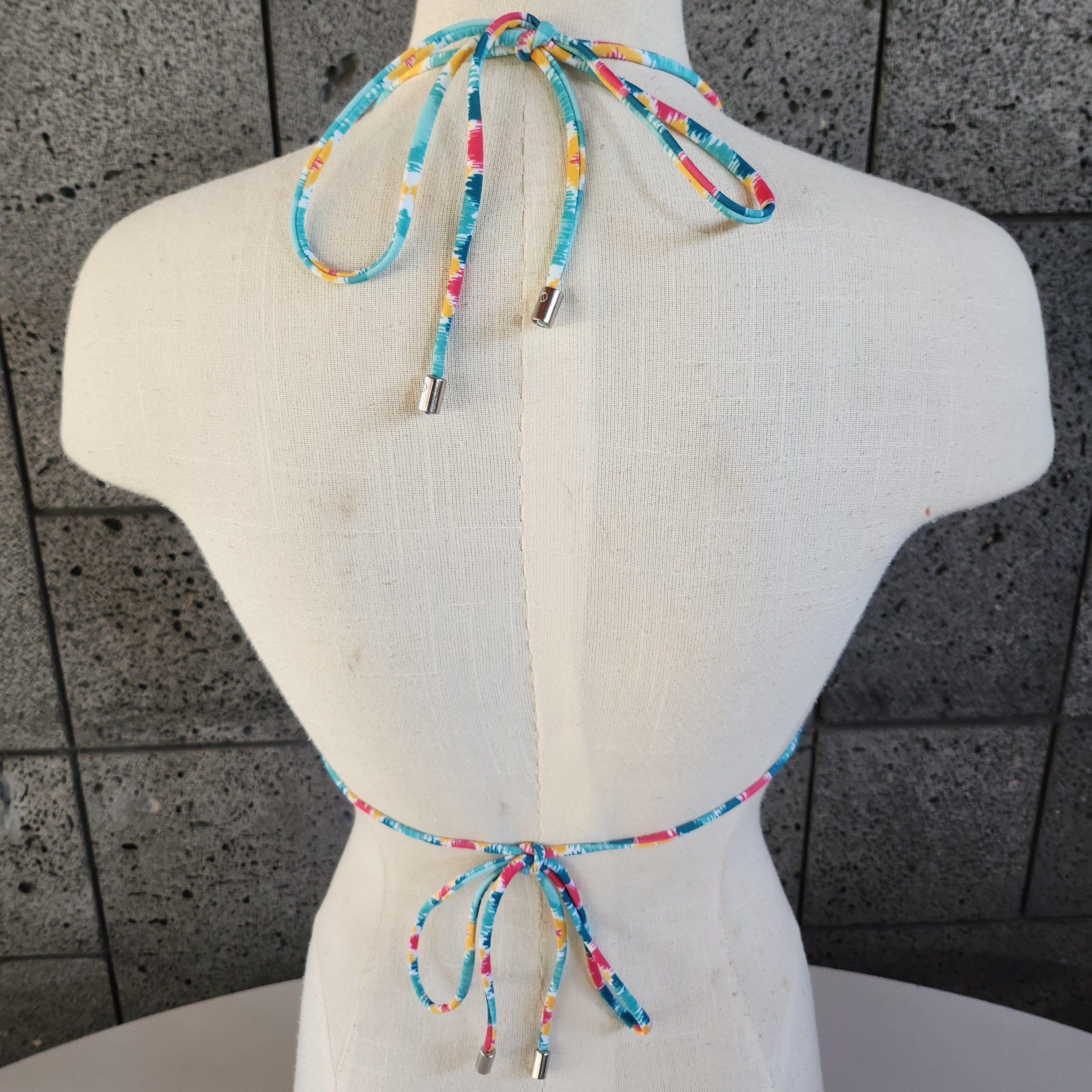 Colorful patterned bikini on a mannequin against a gray tiled floor background