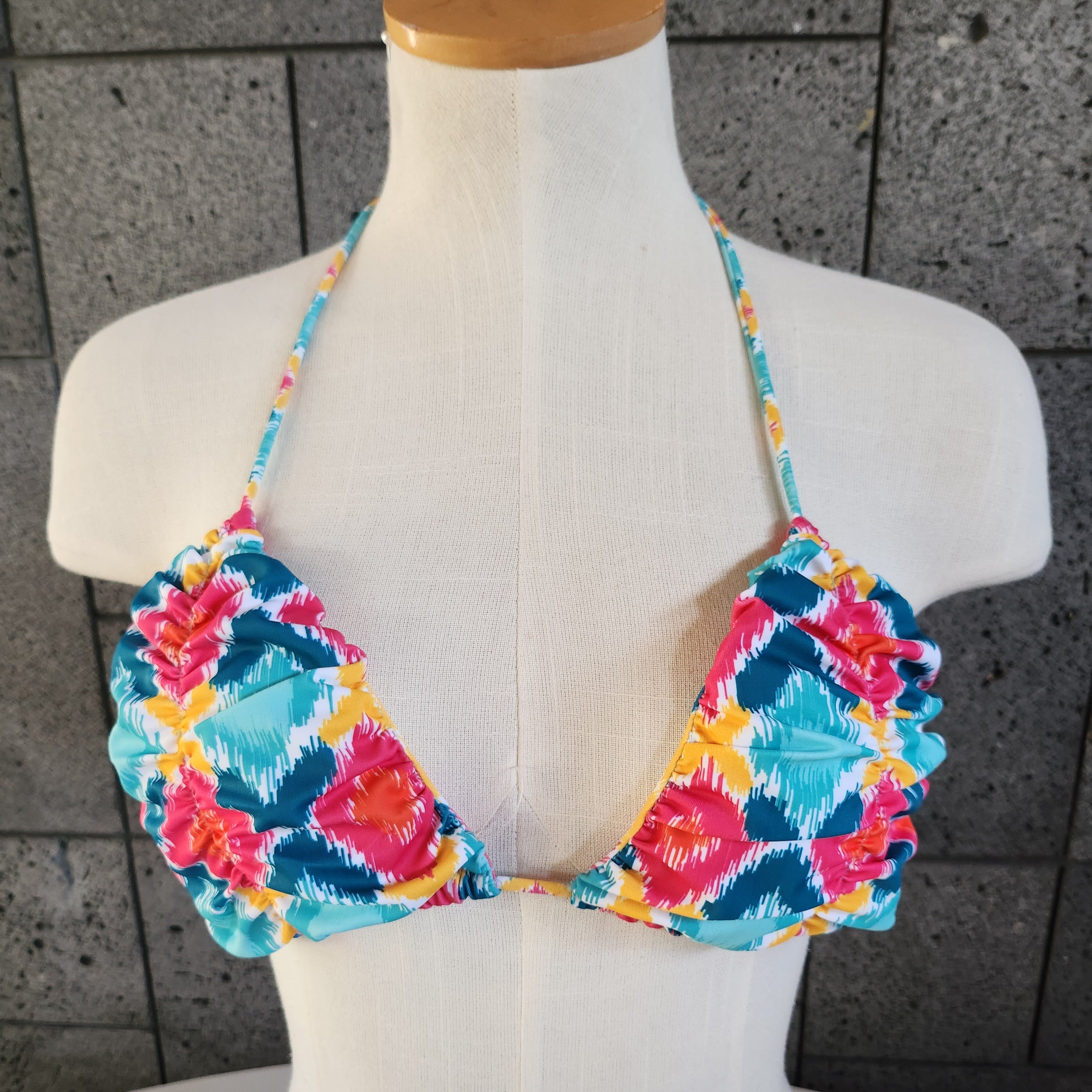 Colorful patterned bikini on a mannequin against a gray tiled floor background