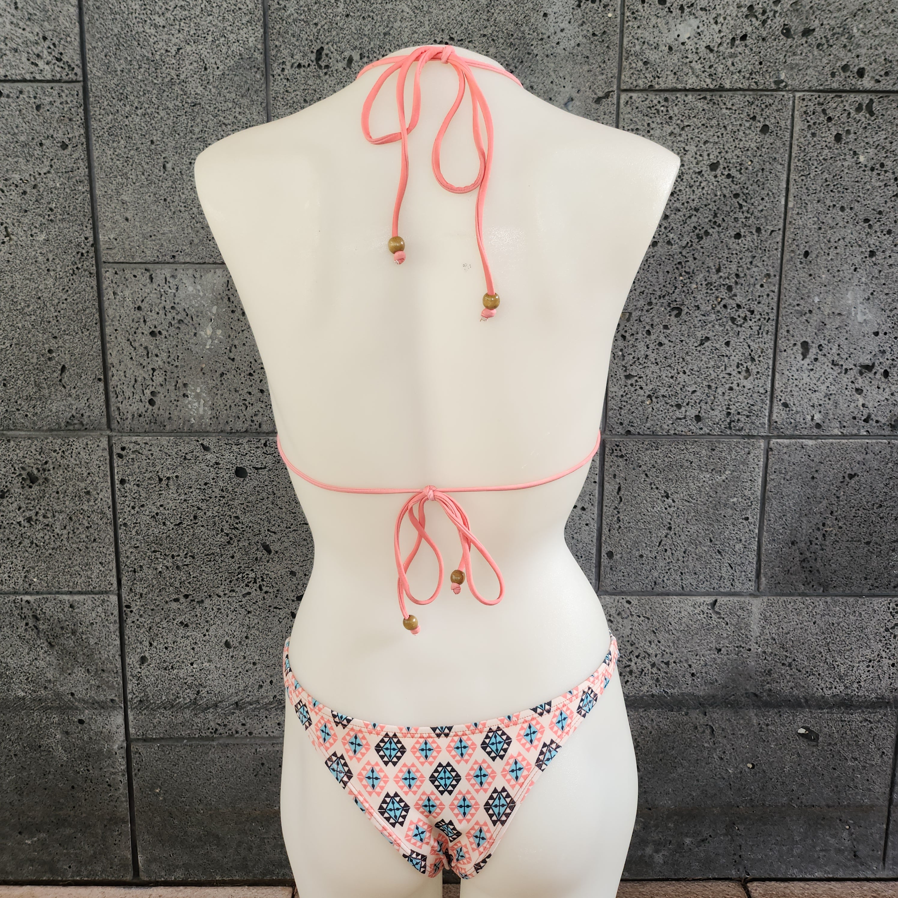 Colorful and geometric patterned monokini on a mannequin against a gray concrete wall.