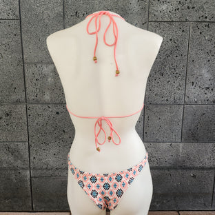 Colorful and geometric patterned monokini on a mannequin against a gray concrete wall.
