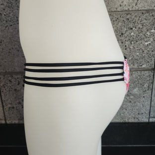 Floral bikini bottom with strappy sides on a mannequin against a gray concrete wall.