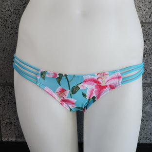 Floral bikini bottom with strappy sides on a mannequin against a gray concrete wall.
