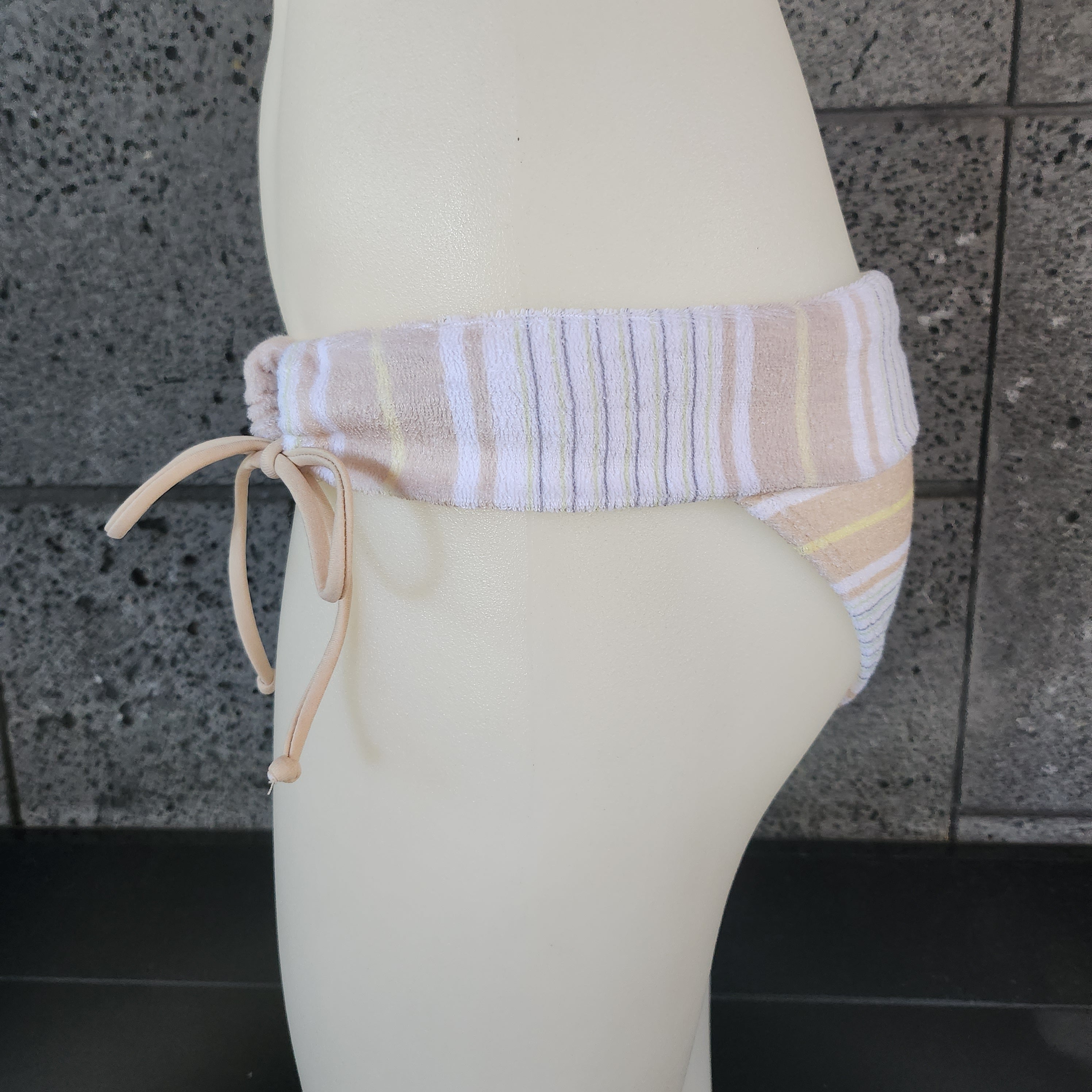 Beige striped towel draped over a white surfboard against a stone wall.