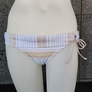 Beige striped towel draped over a white surfboard against a stone wall.