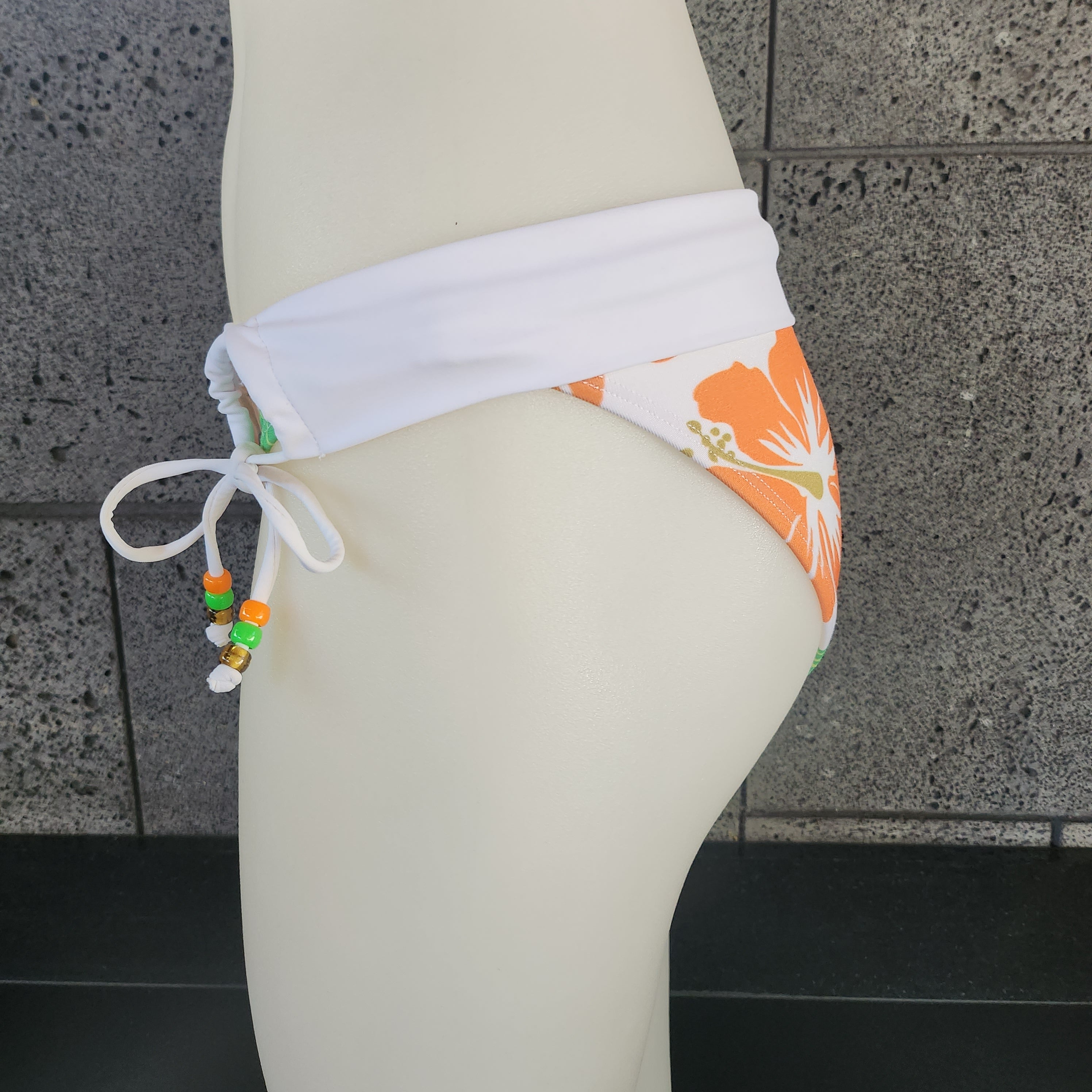 Bikini bottom with blue floral design on a mannequin against a tiled wall.