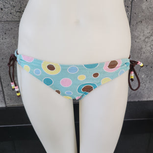 Colorful polka dot bikini bottom on a mannequin against a concrete wall.