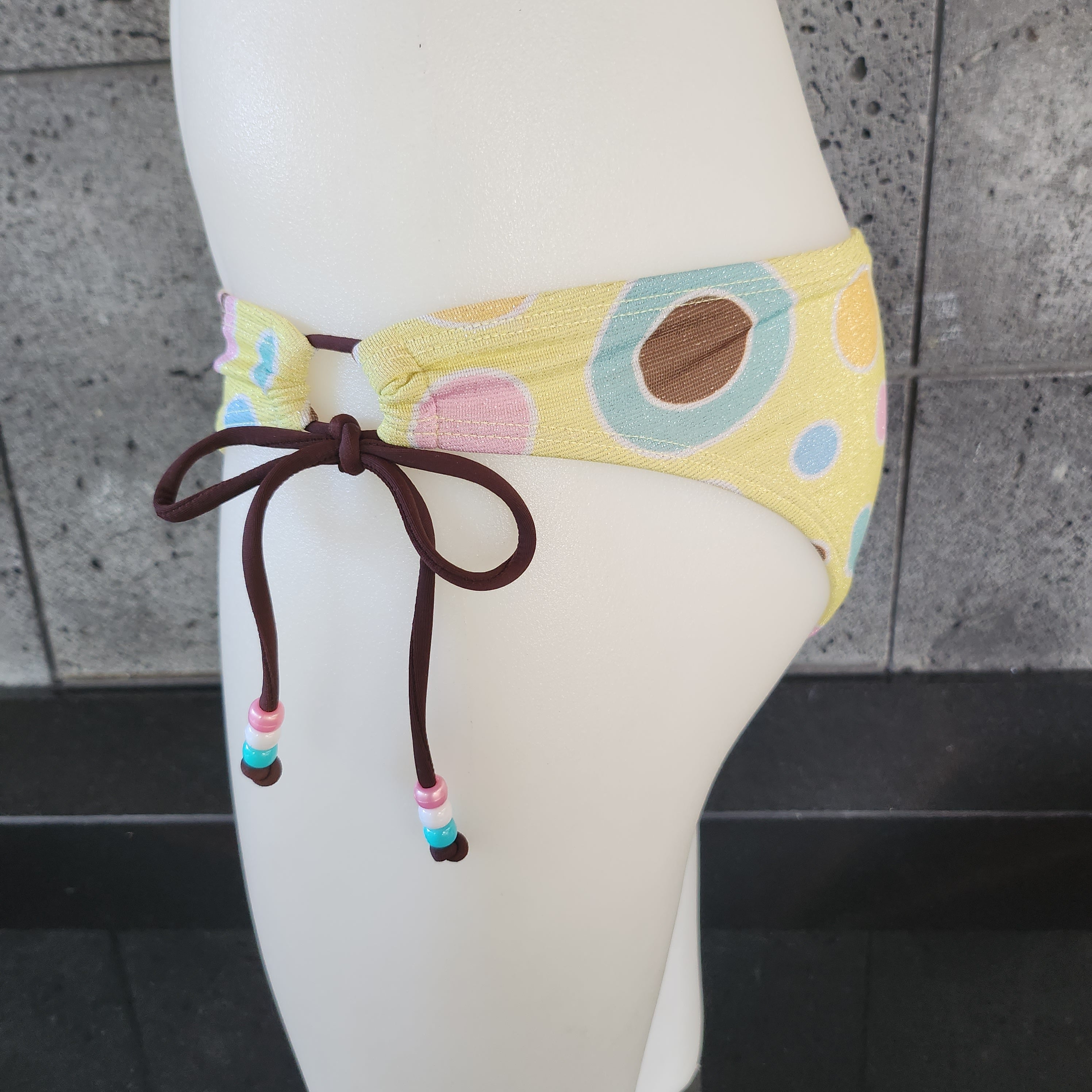 Colorful polka dot bikini bottom on a mannequin against a concrete wall.