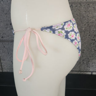 Floral-patterned triangle bikini bottom on a mannequin against a stone wall background