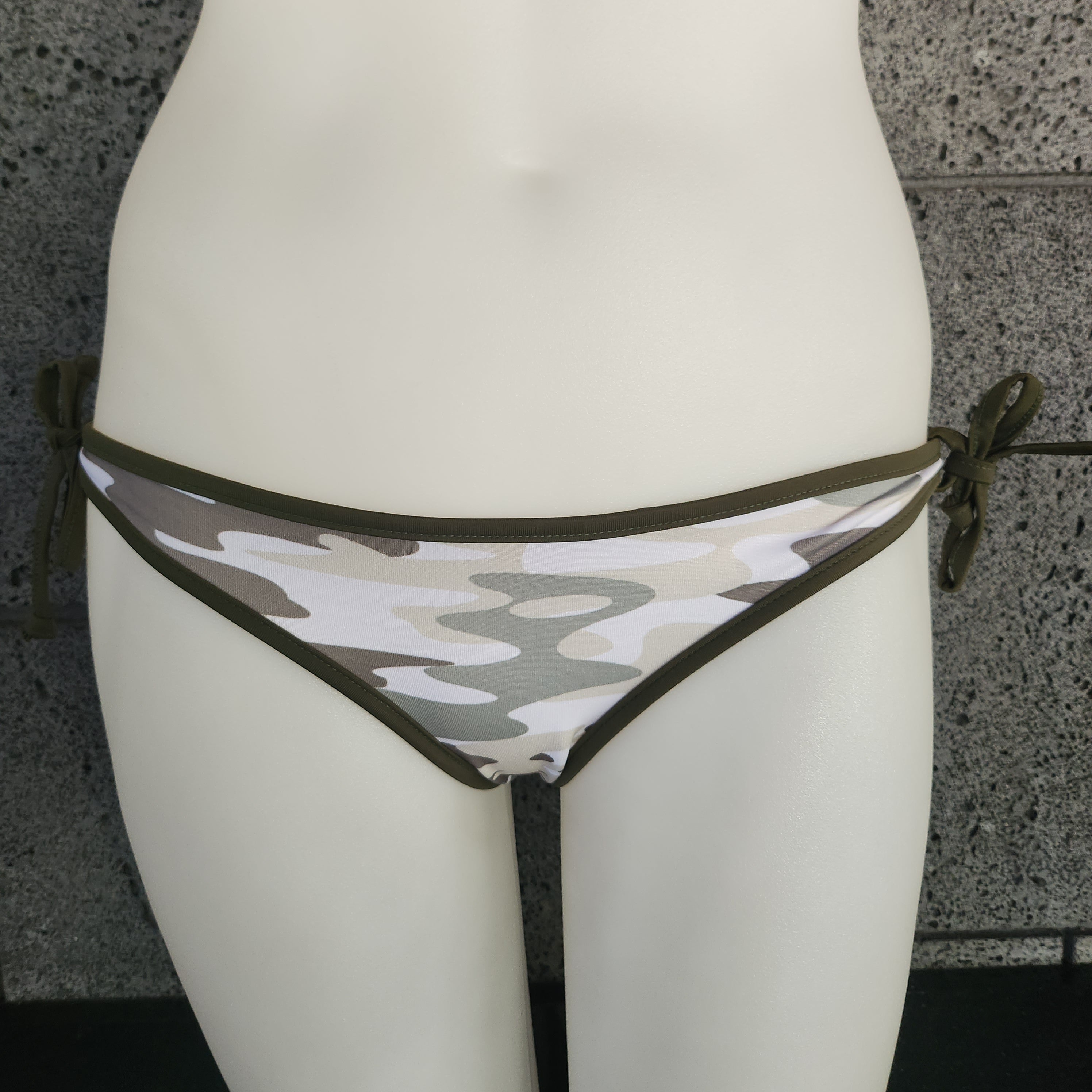 Camouflage-patterned bikini bottom on a mannequin against a gray concrete wall.