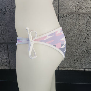 Camouflage-patterned bikini bottom on a mannequin against a gray concrete wall.