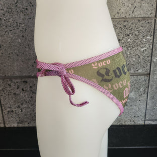 Bikini bottom with sky blue piping and ties on a mannequin against a gray tiled wall.