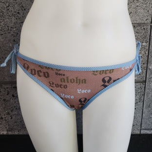 Bikini bottom with sky blue piping and ties on a mannequin against a gray tiled wall.
