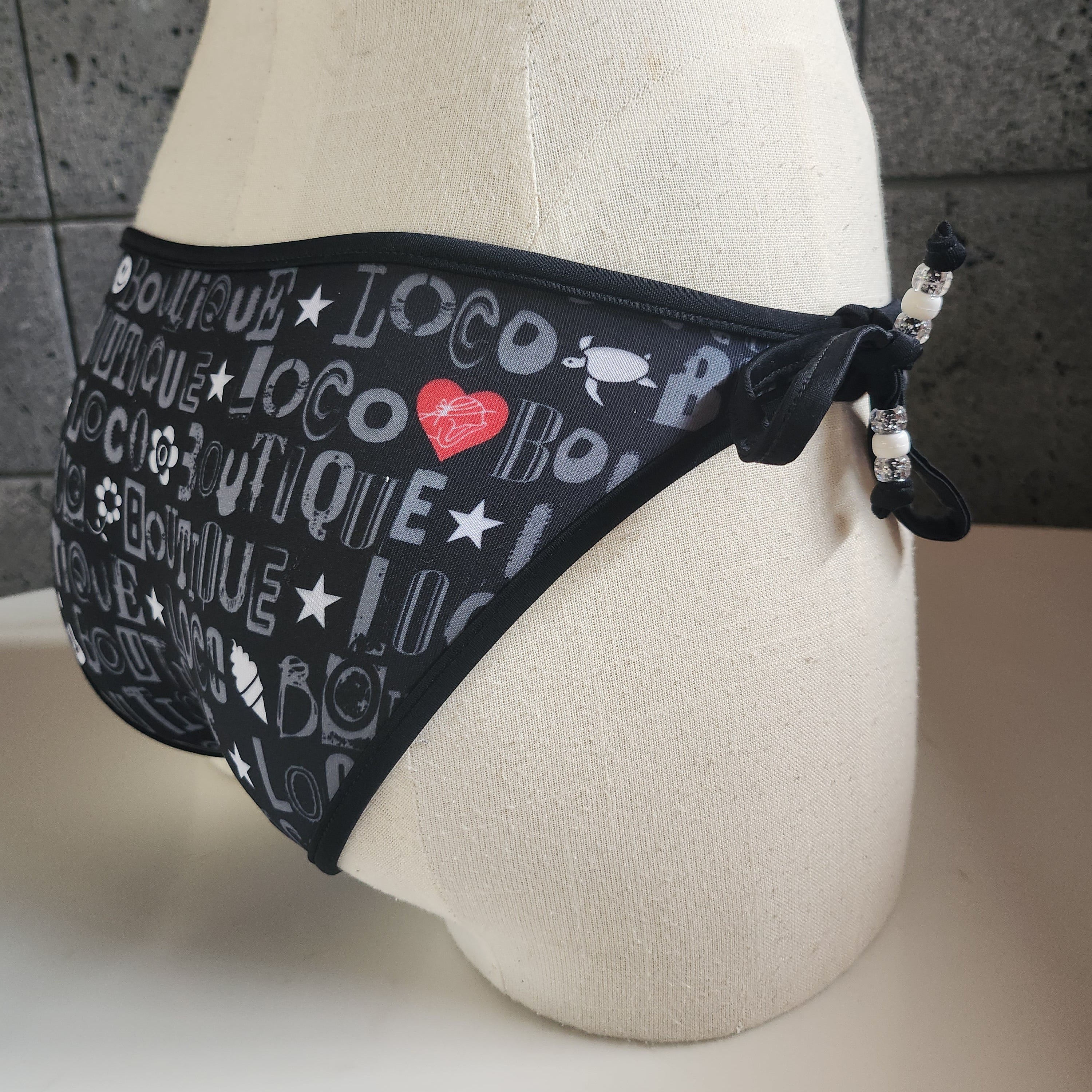 Black bikini bottom with 'Loco Boutique' text on a mannequin against a white background
