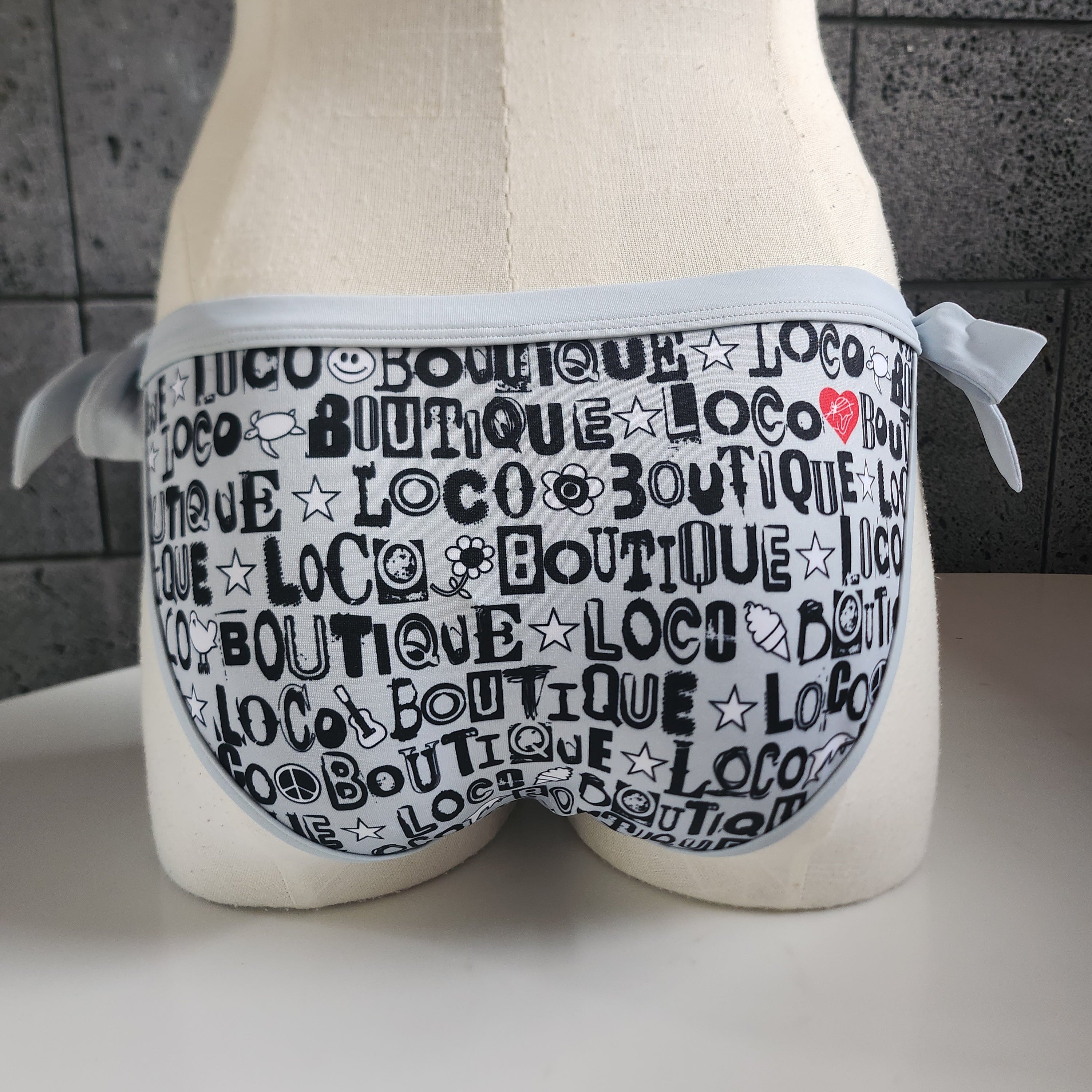 Gray bikini bottom with black text pattern on a mannequin with a neutral background.