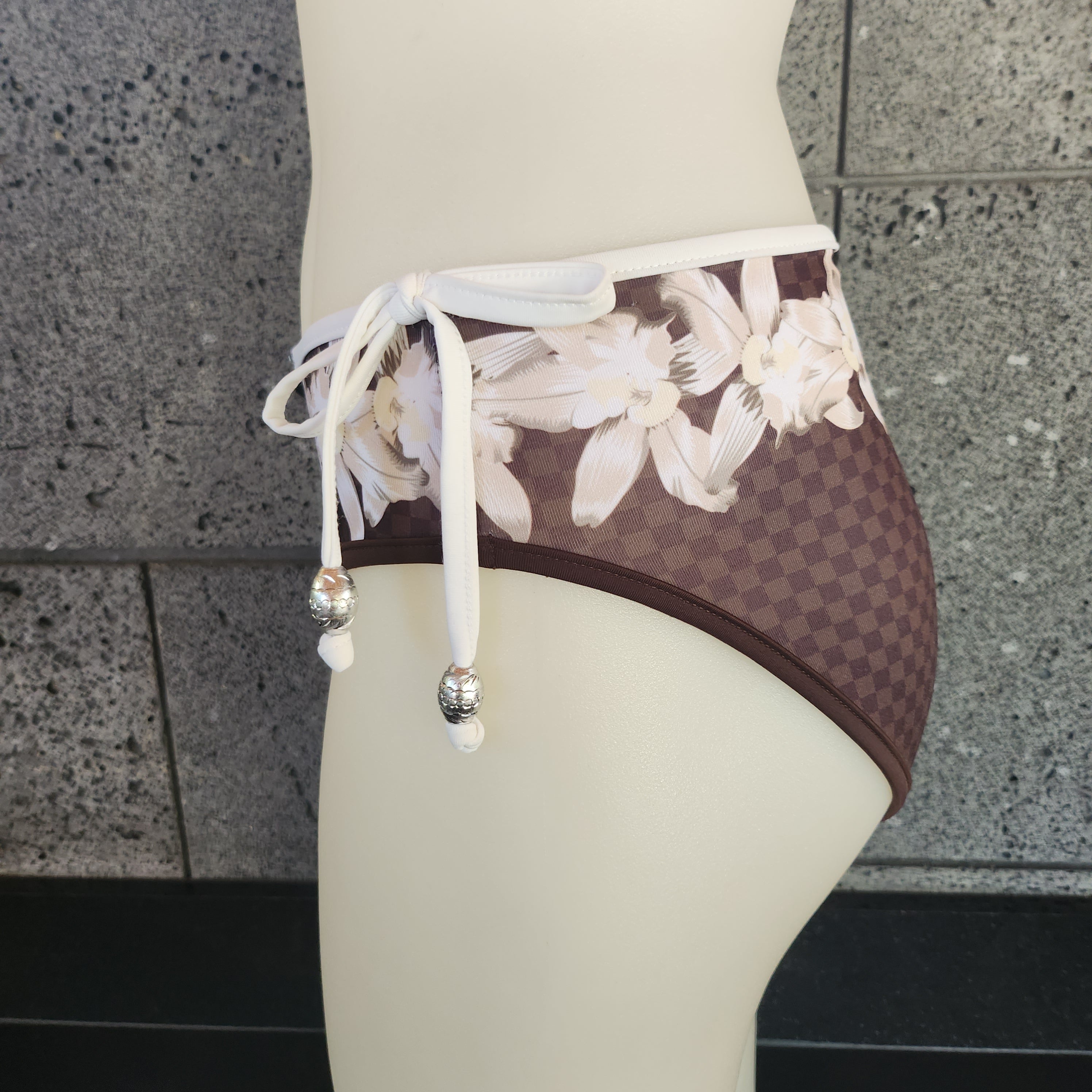 Brown bikini bottom with floral pattern on a mannequin against a gray stone wall.