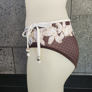 Brown bikini bottom with floral pattern on a mannequin against a gray stone wall.
