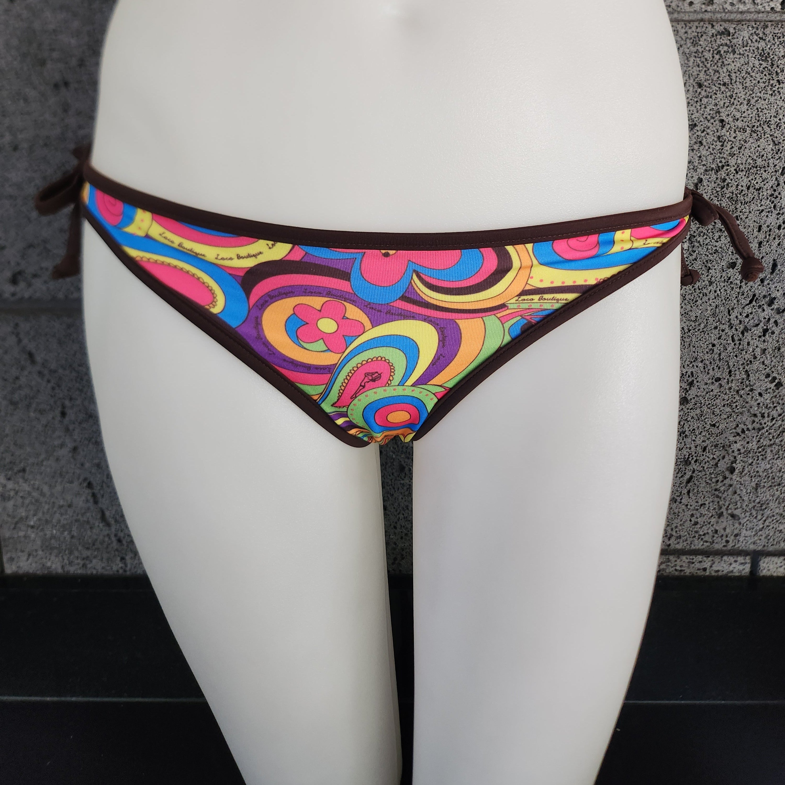 Colorful bikini bottom on a mannequin against a gray wall.
