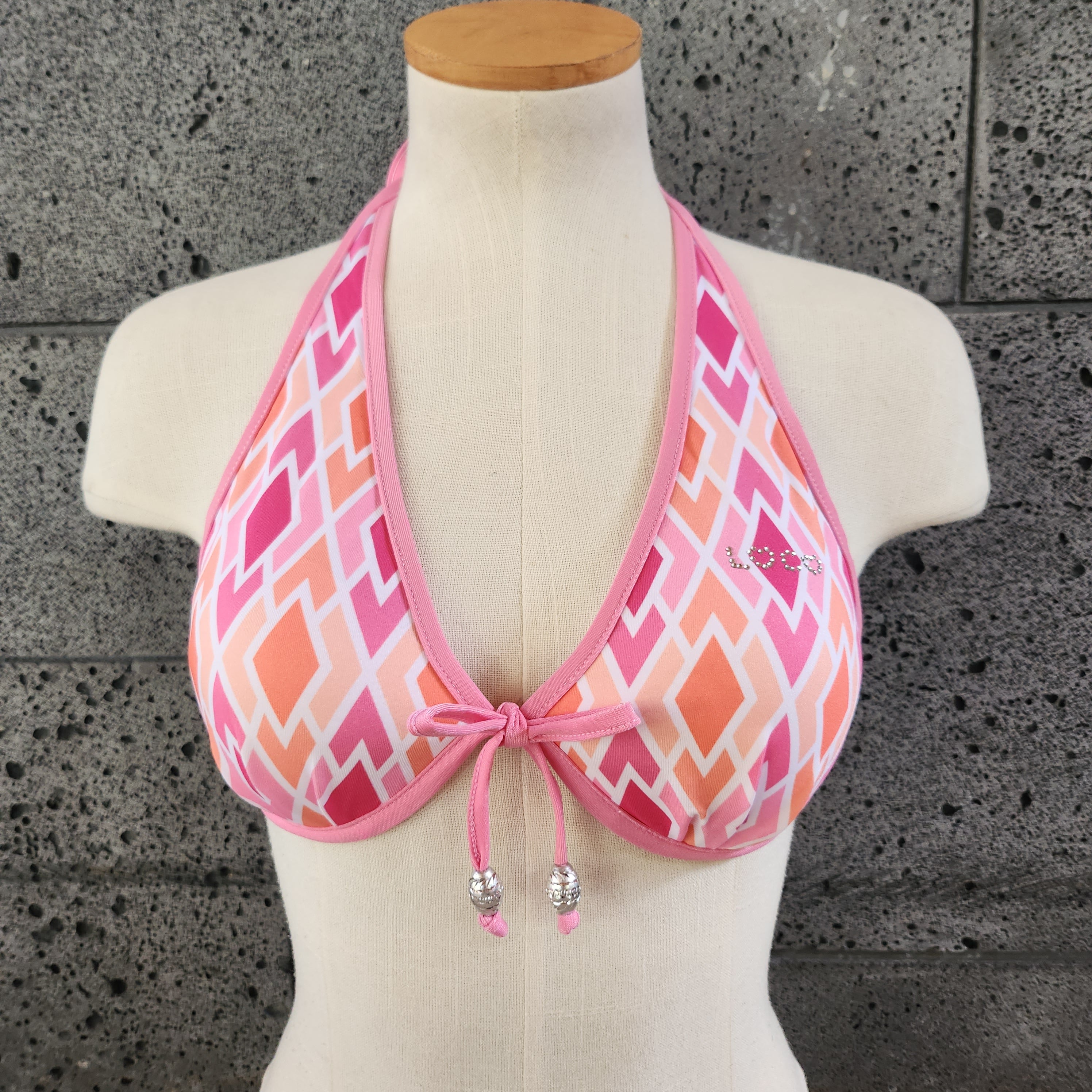 Pink geometric patterned underwire bikini top on a mannequin against a gray concrete background.