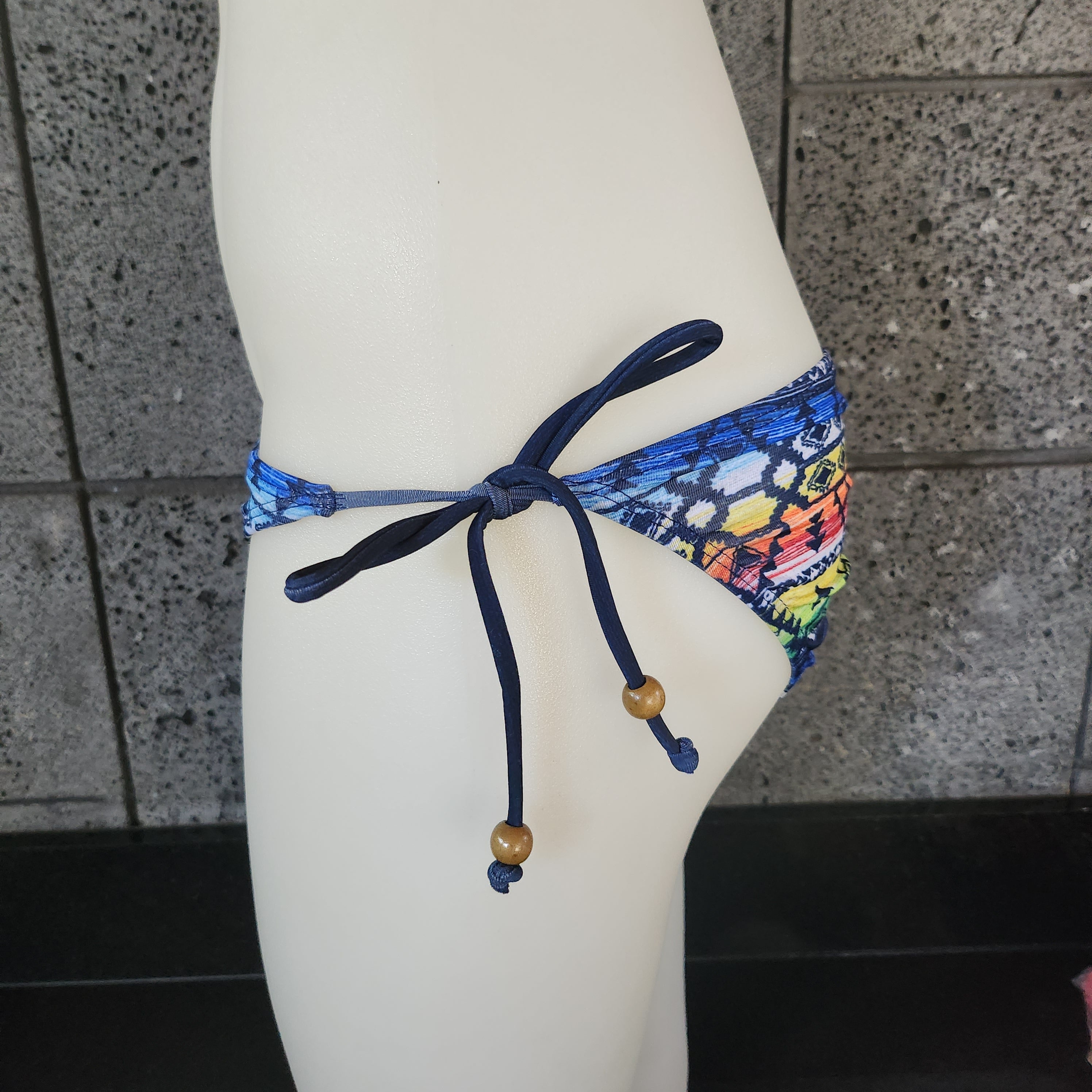 Multicolored patterned bikini bottom on a mannequin against a tiled wall.