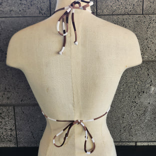 Brown and white checkered bikini top on a mannequin against a tiled wall.