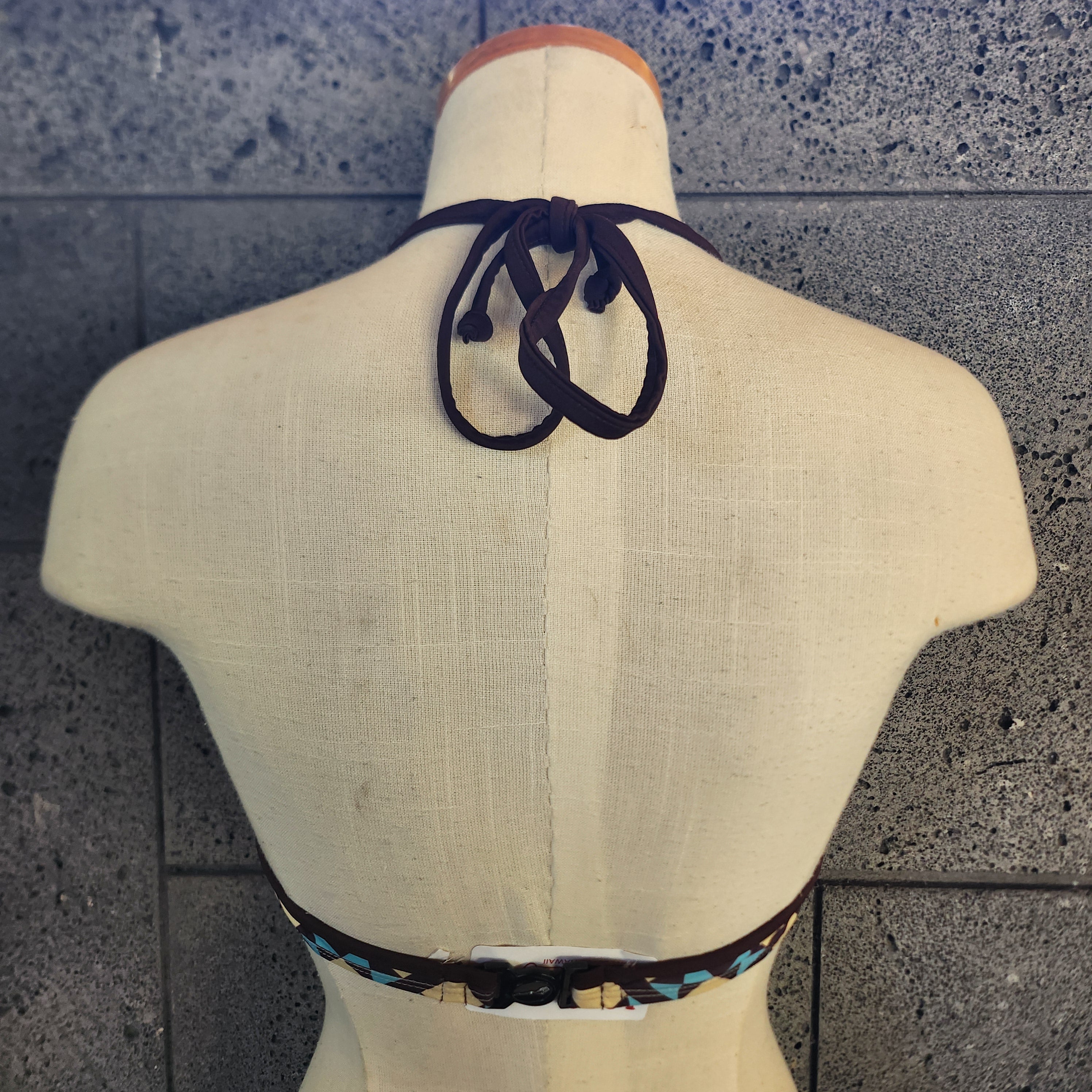 Geometric patterned bikini top on a mannequin against a tiled wall.