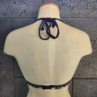 Geometric patterned bikini top on a mannequin against a tiled wall.