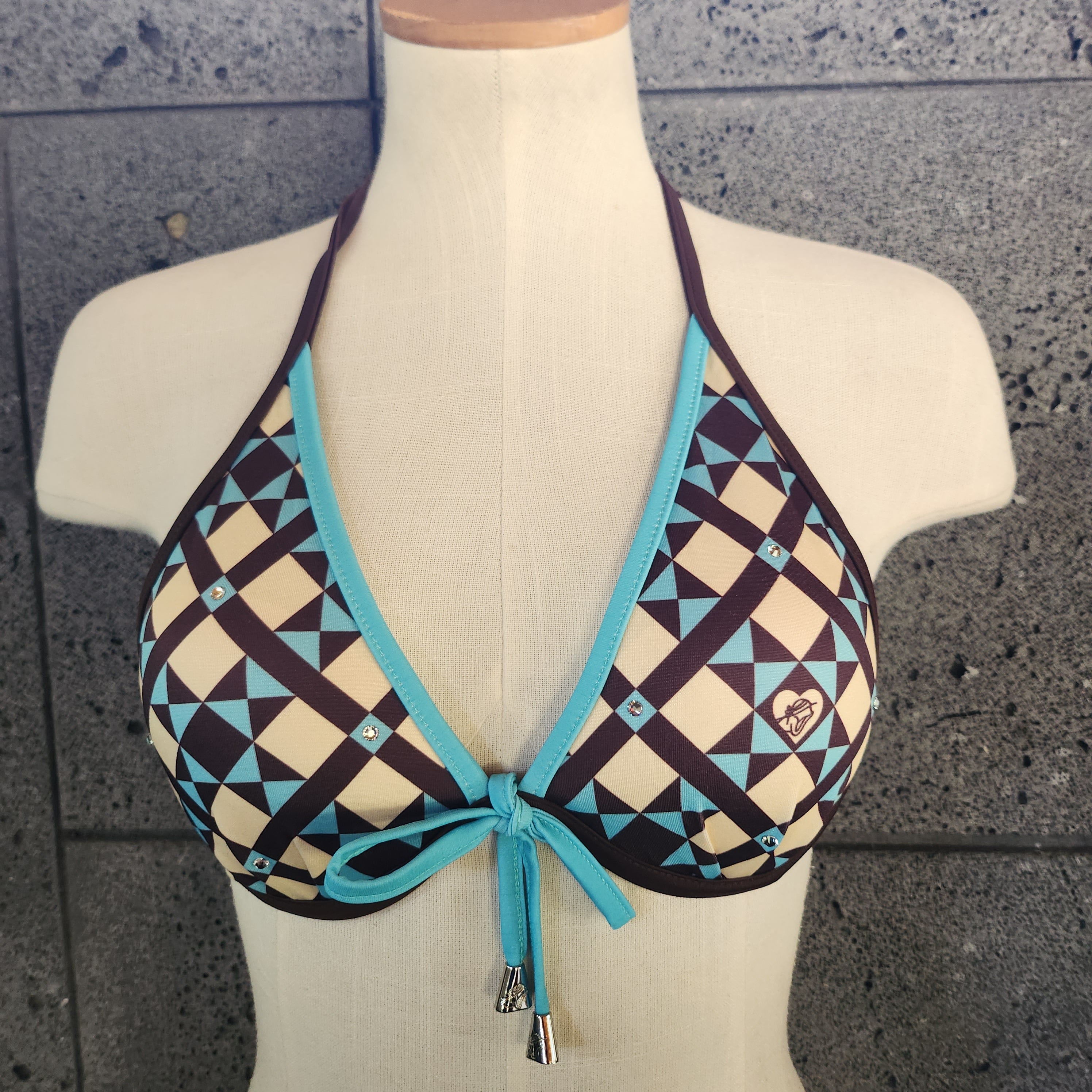 Geometric patterned bikini top on a mannequin against a tiled wall.