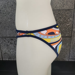 Red bikini bottom with a colorful pattern on a mannequin against a stone wall background
