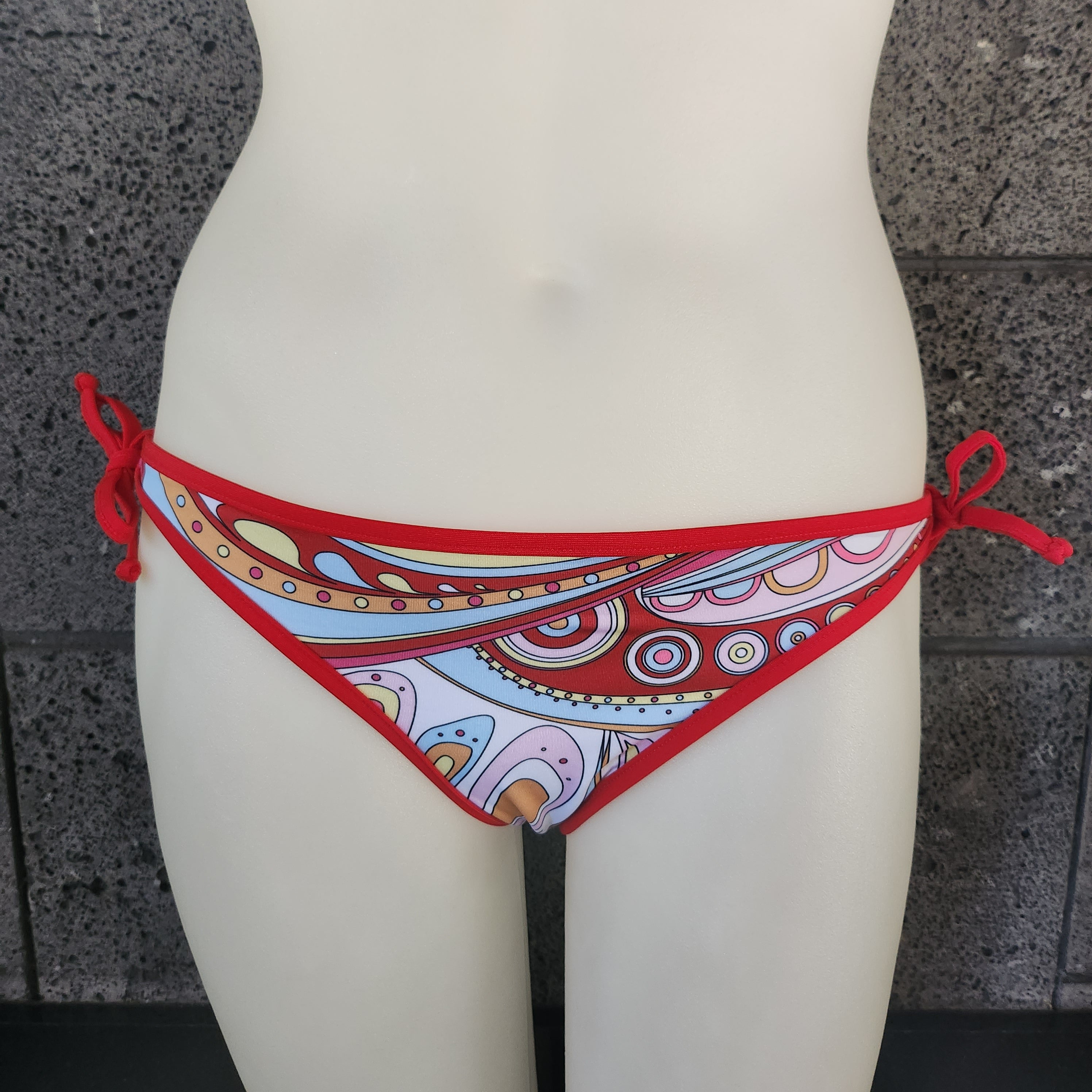 Red bikini bottom with a colorful pattern on a mannequin against a stone wall background