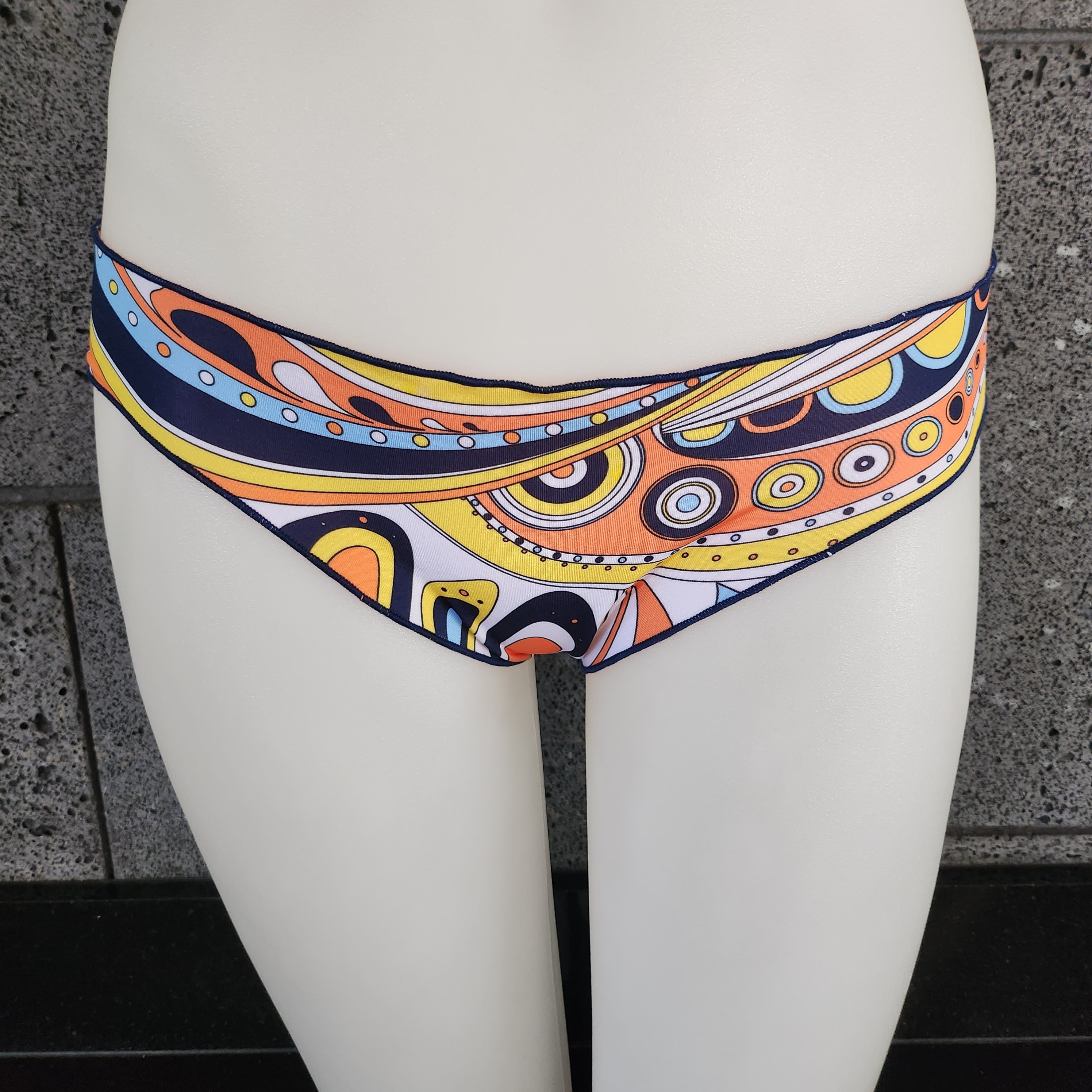 Colorful bikini bottom on a white mannequin against a gray wall.