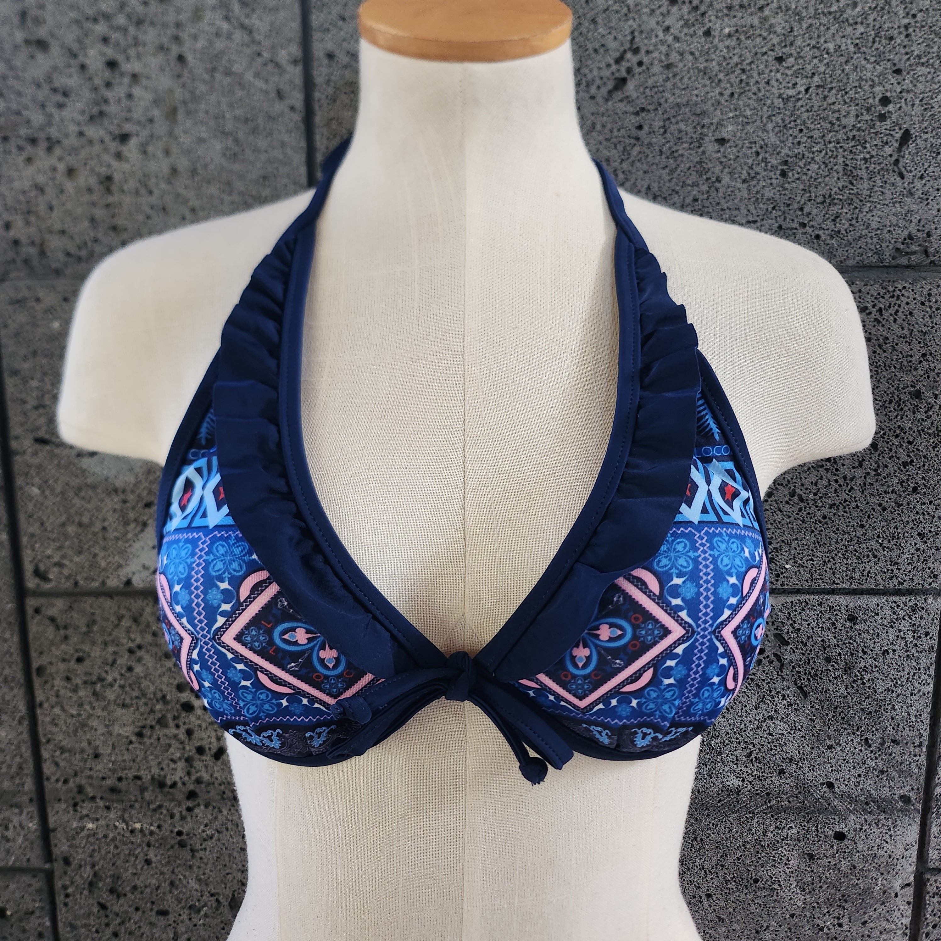 Navy blue bikini top on a mannequin against a gray tiled wall.