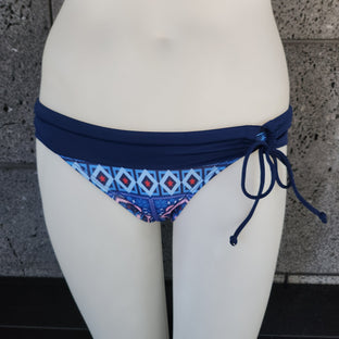 Navy bikini bottom with geometric pattern on a mannequin against a concrete wall.
