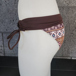 Navy bikini bottom with geometric pattern on a mannequin against a concrete wall.