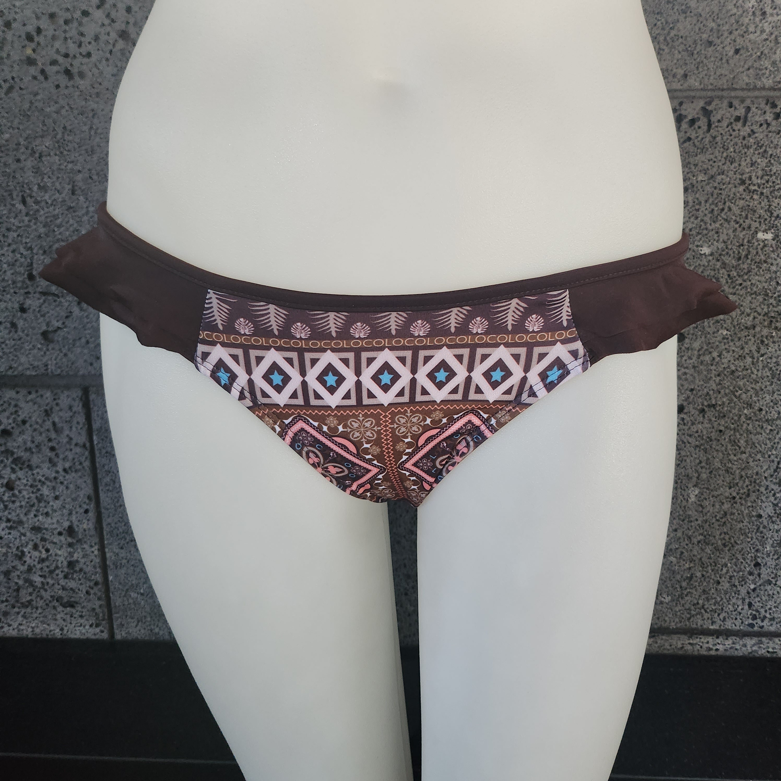 Brown bikini bottom with geometric pattern on a mannequin against a gray wall.
