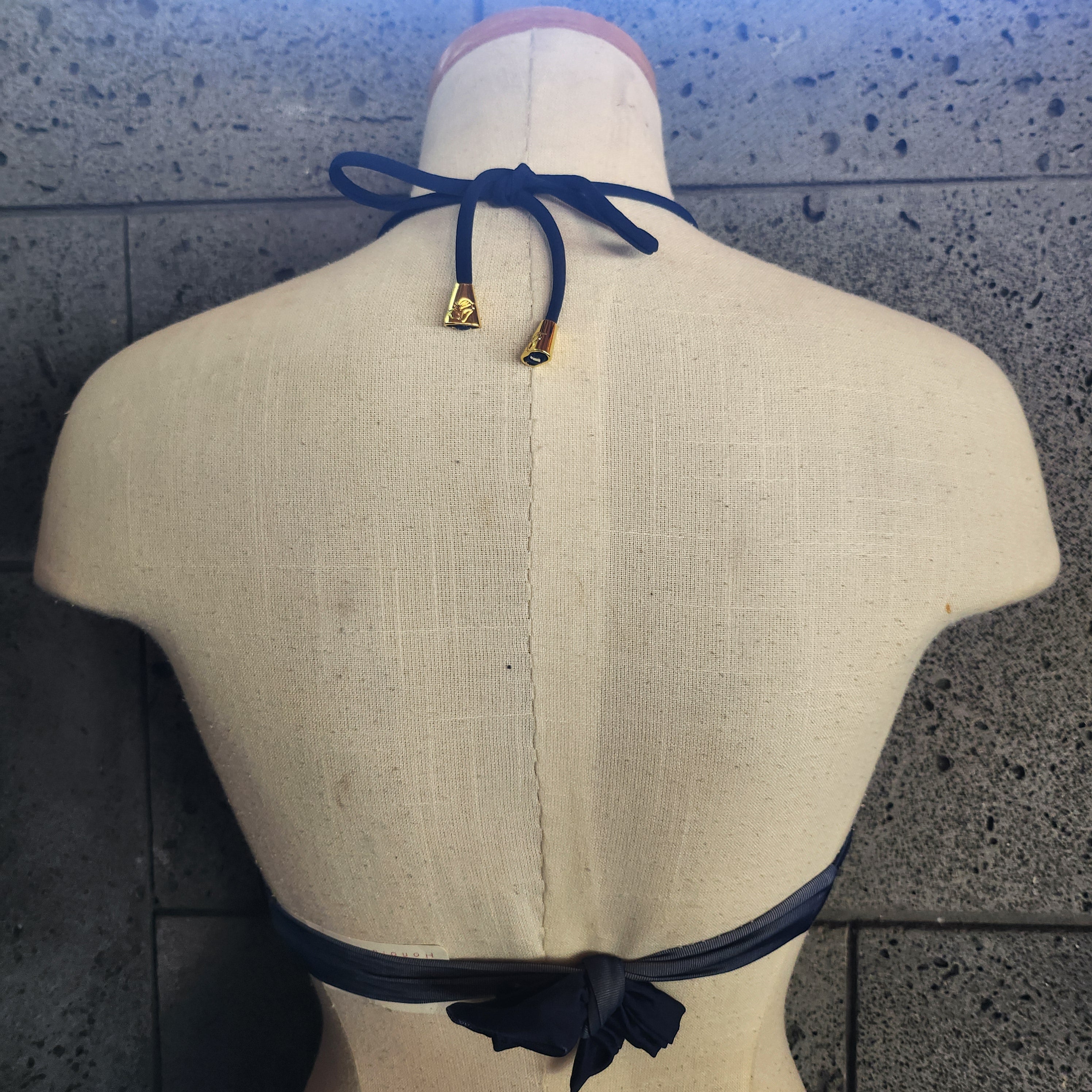 Bikini top with chain pattern on a mannequin against a textured wall.