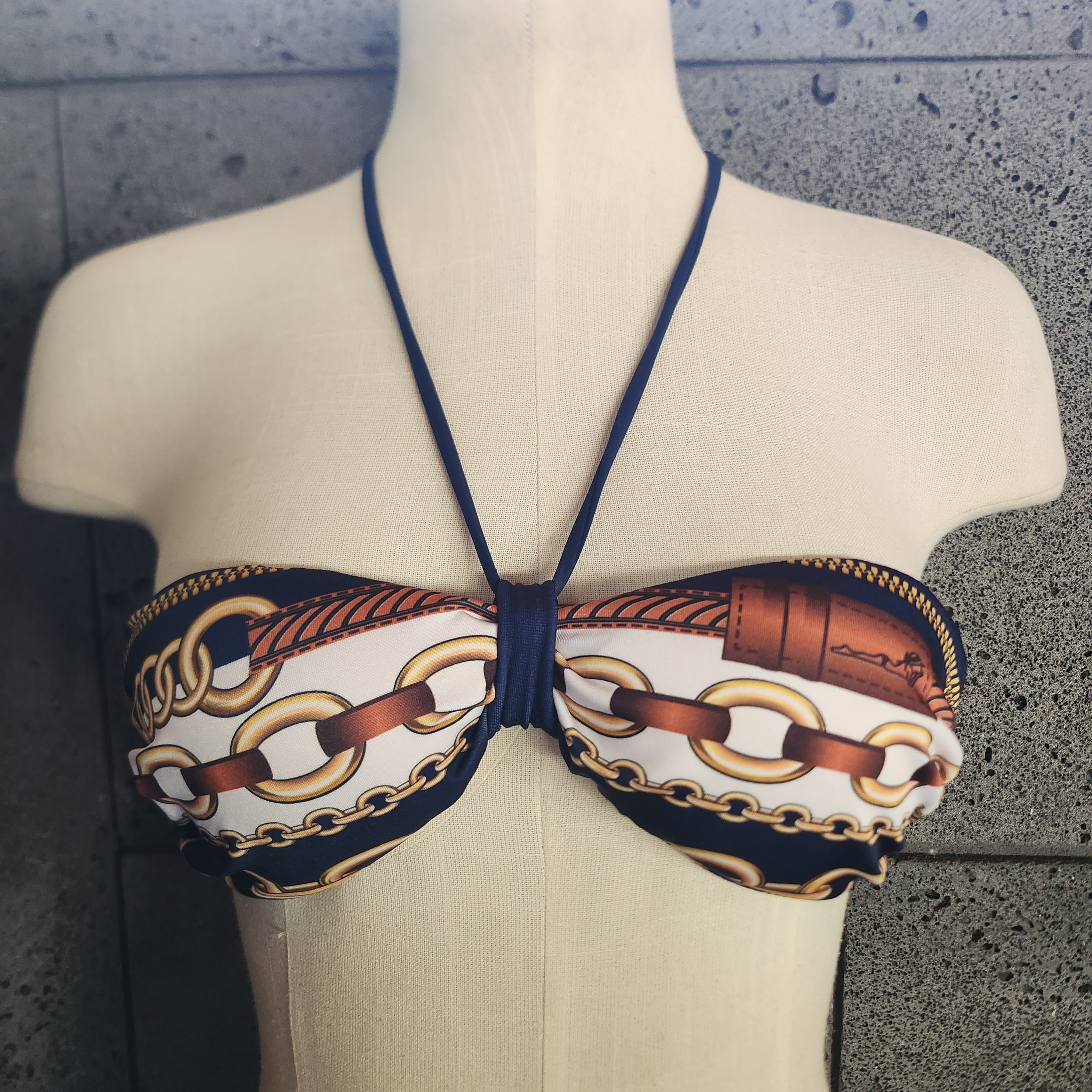 Bikini top with chain pattern on a mannequin against a textured wall.