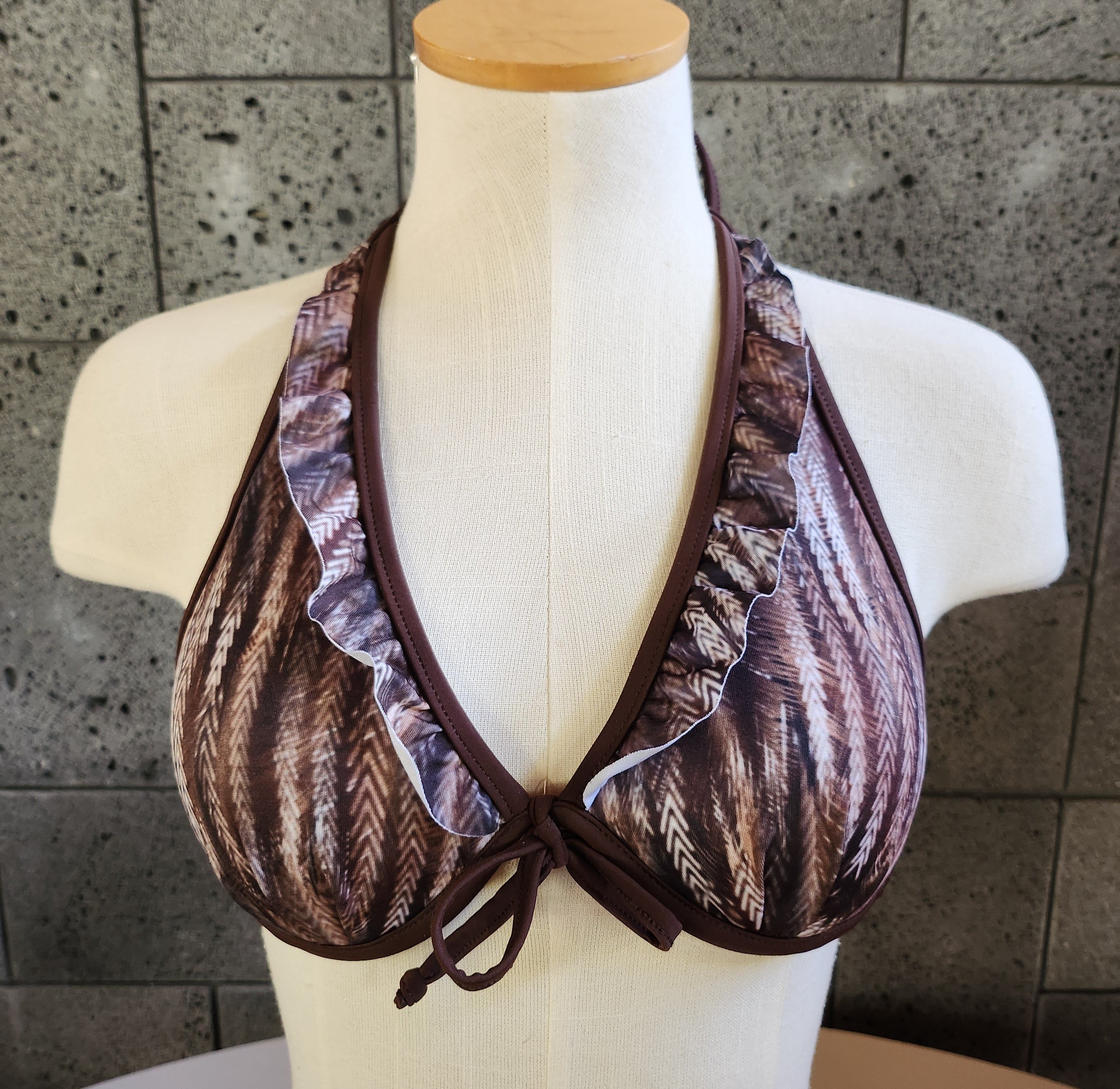Brown patterned bikini top on a mannequin against a tiled wall.