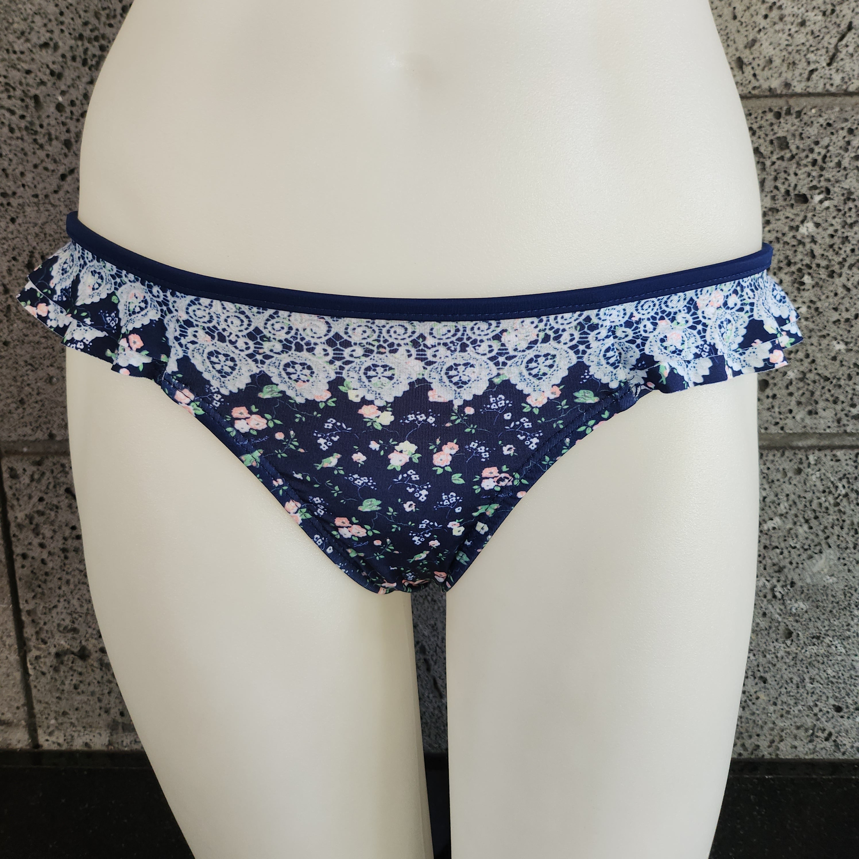 Navy blue floral-patterned bikini bottom on a mannequin against a stone wall.