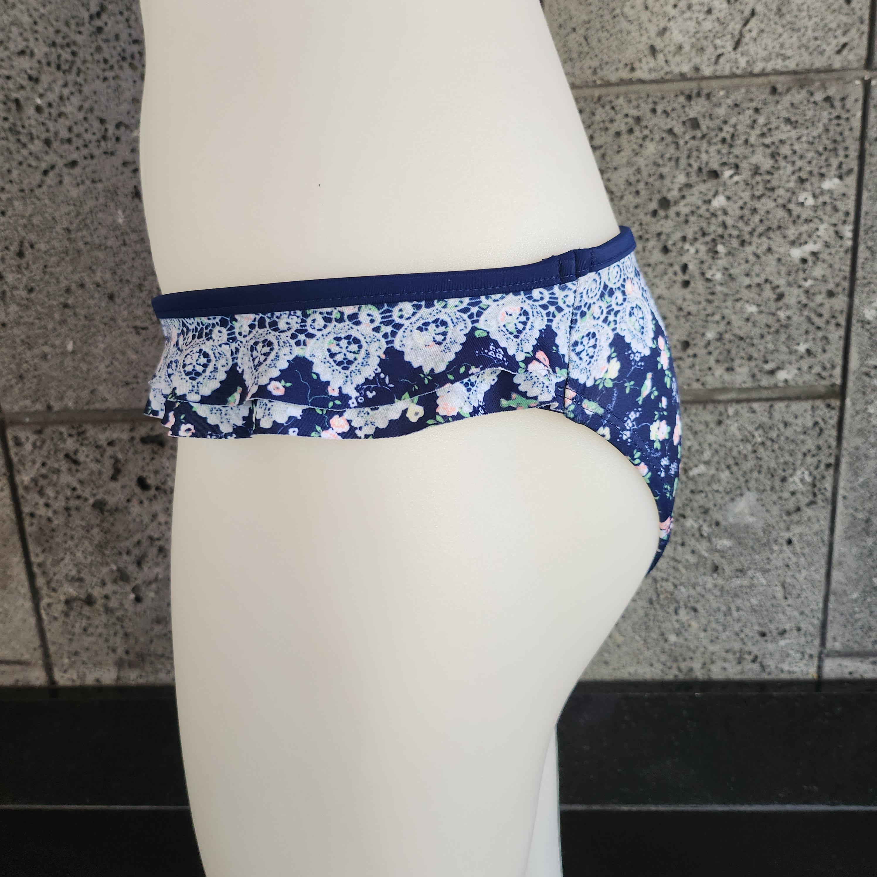 Navy blue floral-patterned bikini bottom on a mannequin against a stone wall.