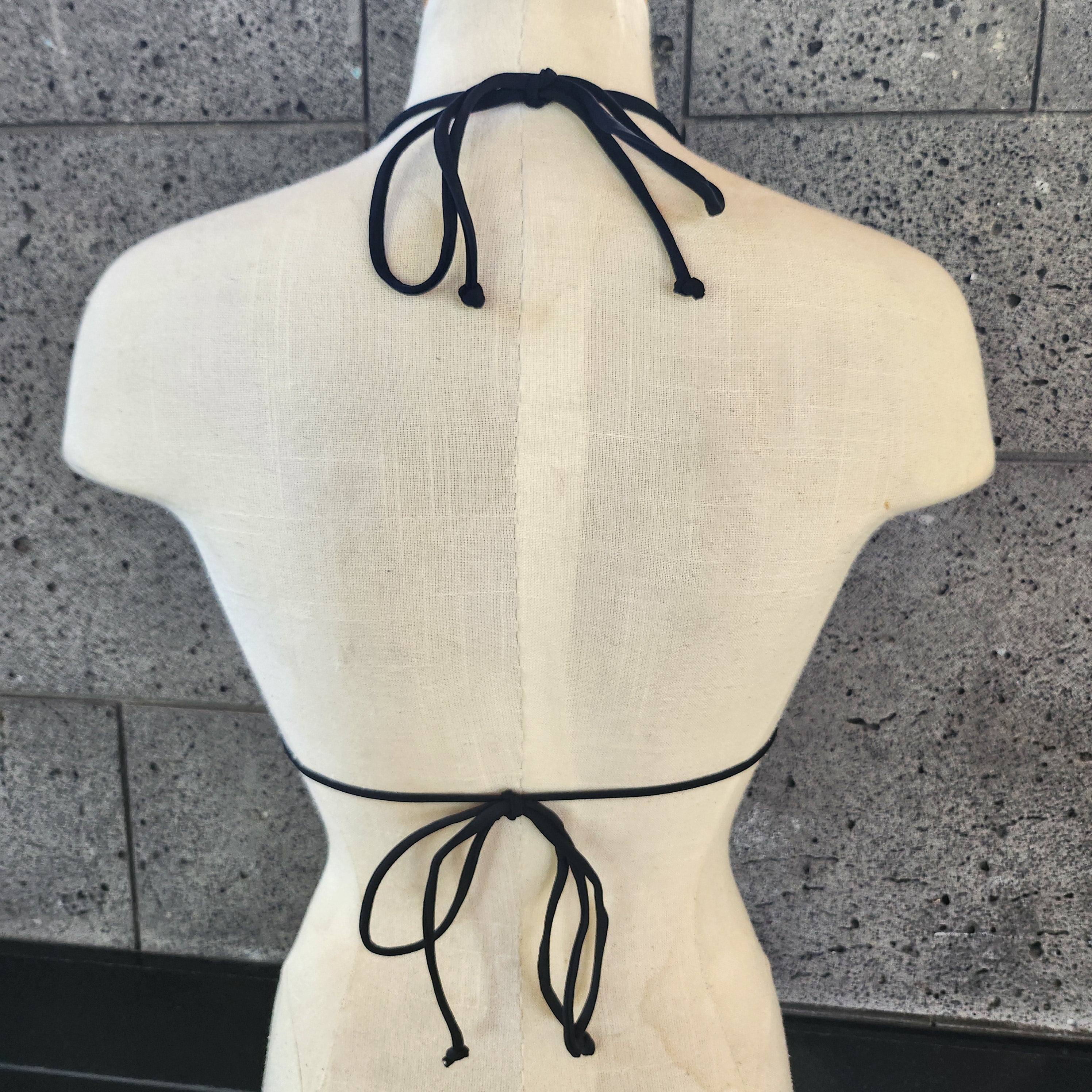 Mint bikini top with geometric pattern on a mannequin against a stone wall.