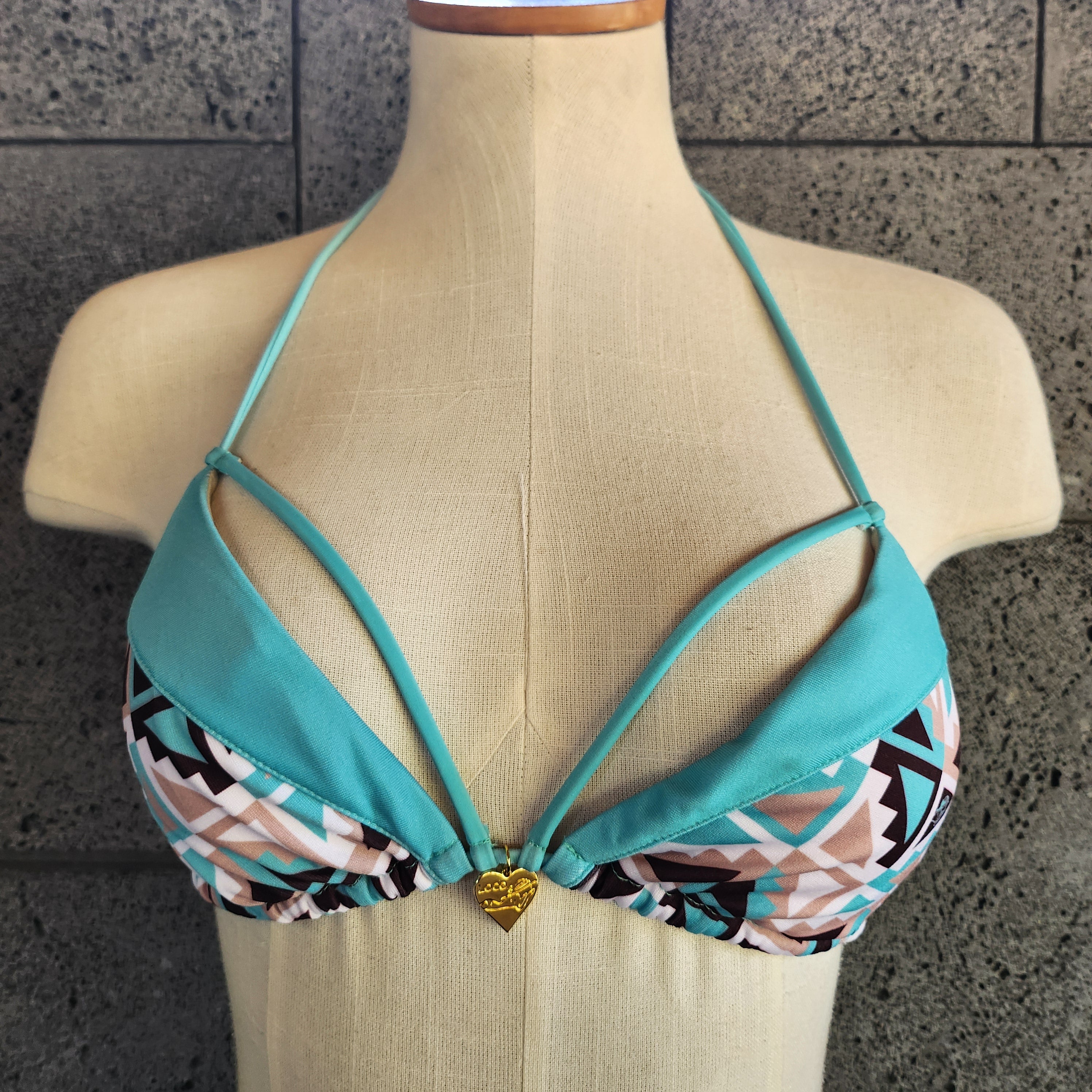 Mint bikini top with geometric pattern on a mannequin against a stone wall.