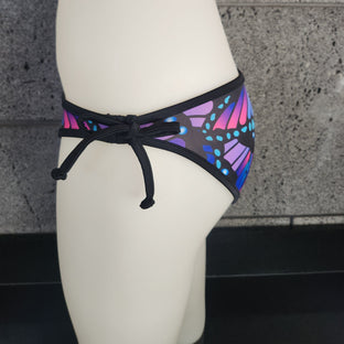 Multicolored butterfly-patterned bikini bottom on a mannequin against a gray textured wall.