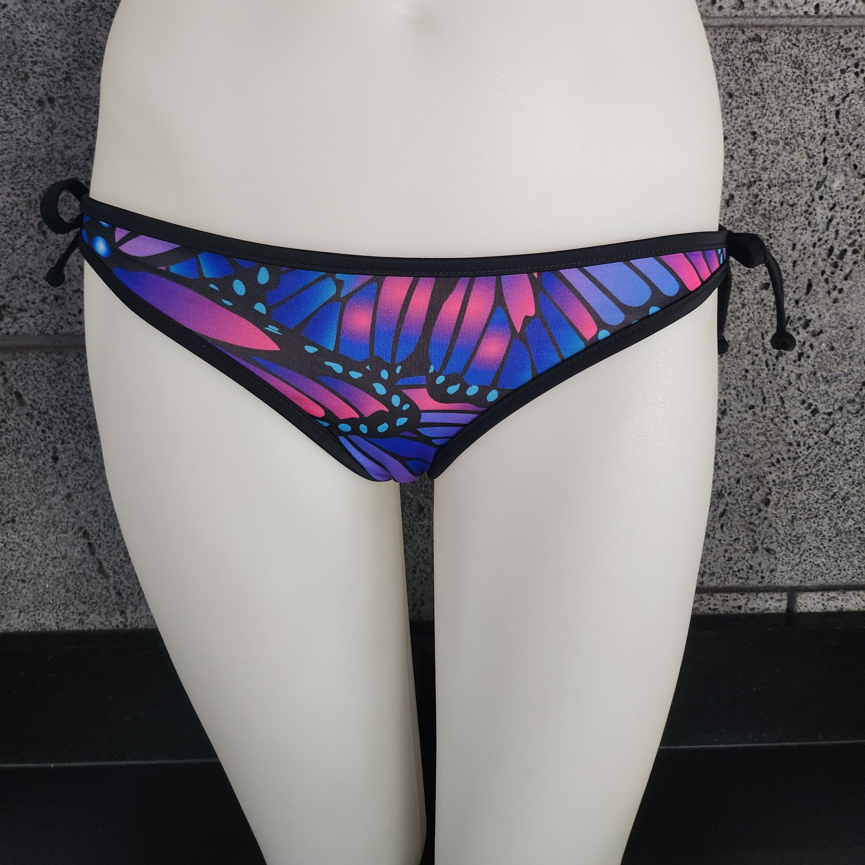 Multicolored butterfly-patterned bikini bottom on a mannequin against a gray textured wall.