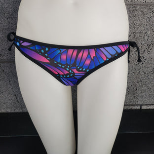 Multicolored butterfly-patterned bikini bottom on a mannequin against a gray textured wall.