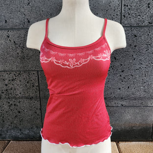 Red tankini top with embroidery details on a mannequin against a textured wall.