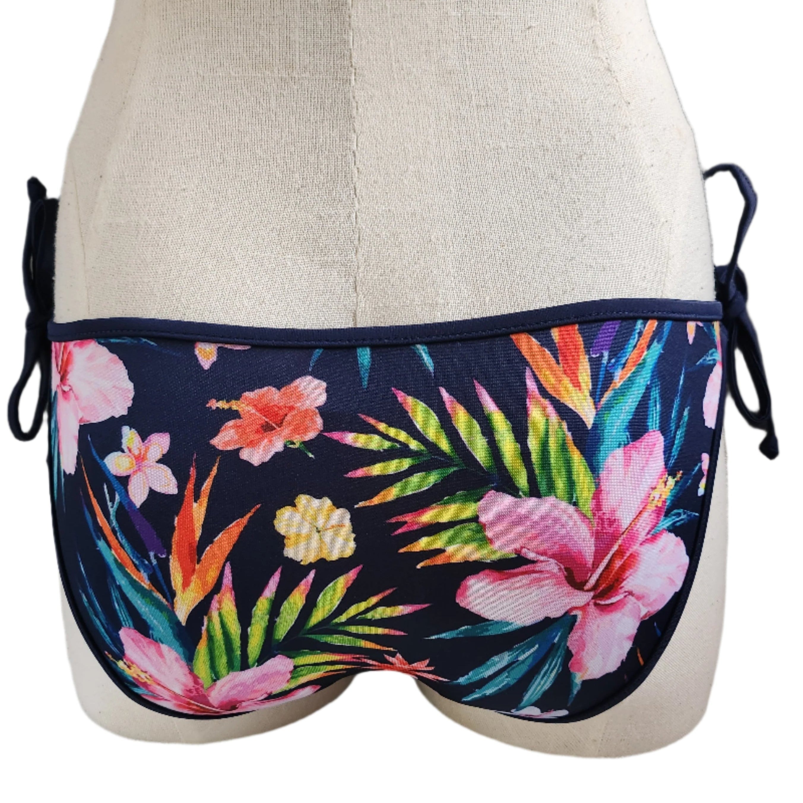 A swimwear bottom with a vibrant floral print and a removable bow detail, displayed on a mannequin.