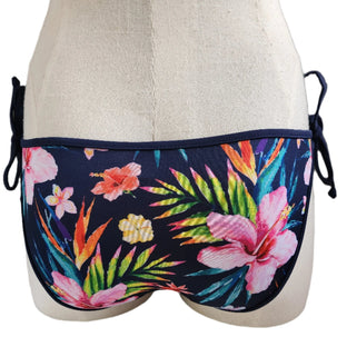 A swimwear bottom with a vibrant floral print and a removable bow detail, displayed on a mannequin.